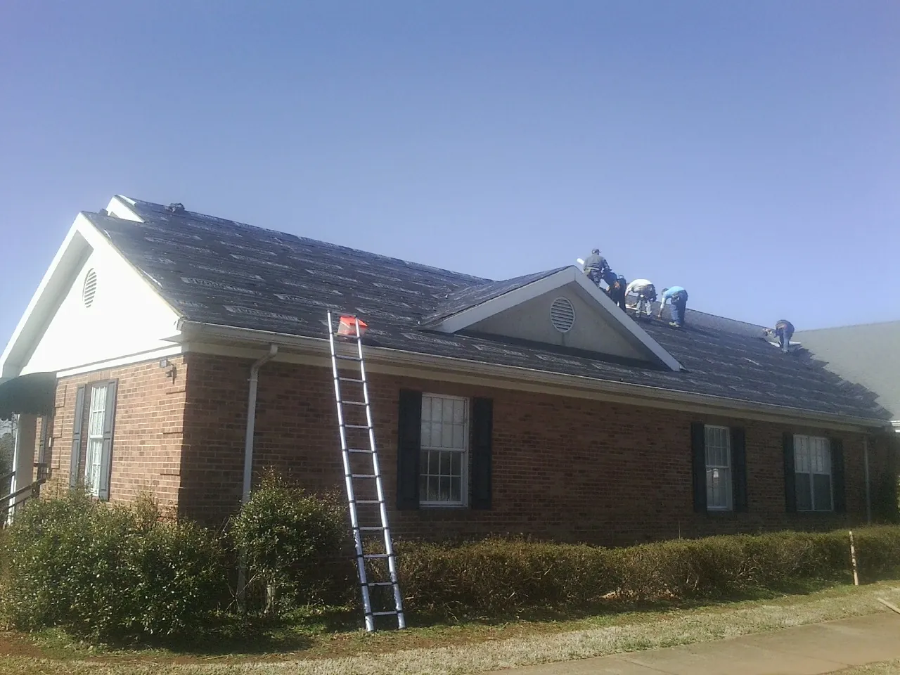 Crew tearing shingles off a brick ranch roof with a ladder set — Emergency Roof Repair work by our crew in Jackson