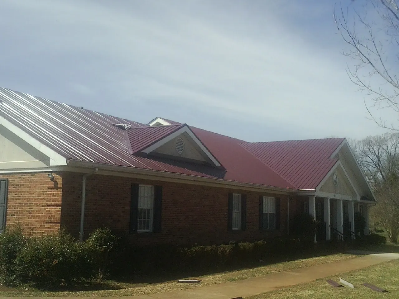 Red metal roof with gabled entries on a long brick building, from a Hail Damage Roof Repair job in Jackson