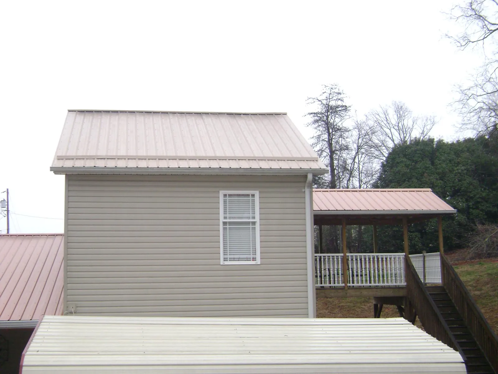 Tan metal roofs on a two story addition and attached porch, from a Roof Replacement job in Jackson